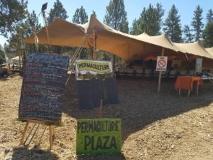 Tent at a festival with signs reading Permaculture Plaza